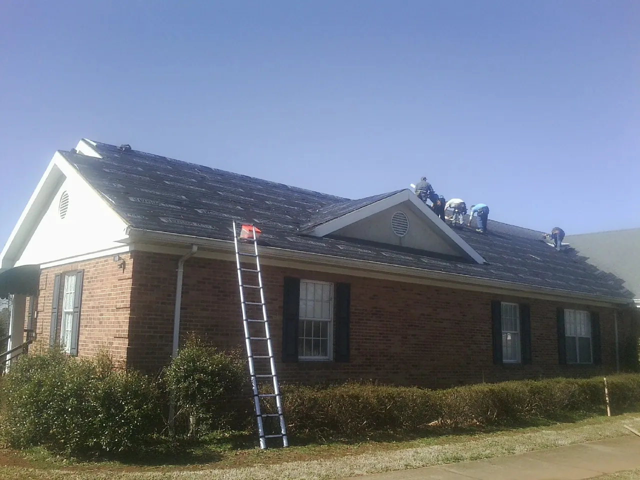 Crew tearing shingles off a brick ranch roof with a ladder set — Metal Roof Repair work by our crew in Columbia City