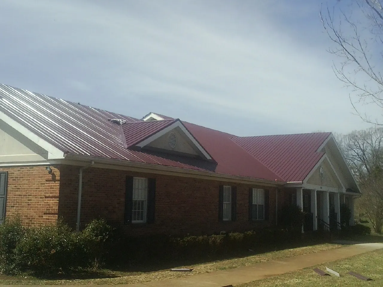 Red metal roof with gabled entries on a long brick building, from a Hail Damage Roof Repair job in Columbia City